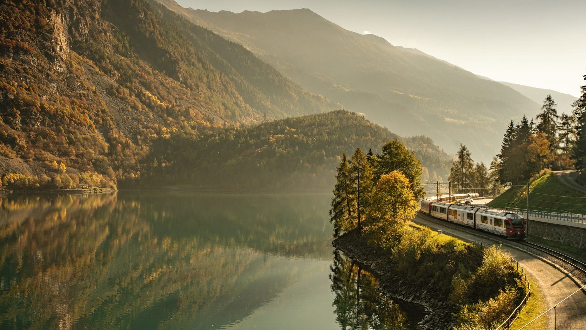Swiss train running along an alpine lake in autumn